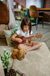 Little girl playing ukulele sitting on carpet next to handmade shelter tent in living room. Concentrated child practicing music next to diy teepee. Vacation camping at home or staycation concept.