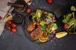 pieces of Organic grilled Tuna Steak on black ceramic serving dish with salad on a table