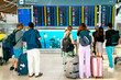 Group of travelers, adorned with backpacks and luggage, stands before an airport departure board, eagerly checking their flight status, a scene capturing the essence of modern travel