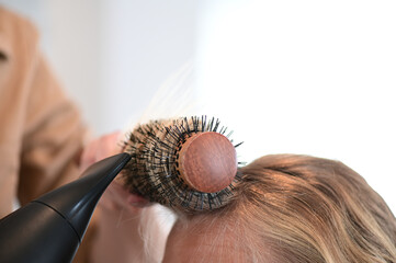 Hair stylist using a hair dryer and a brush on a blonde client in a modern salon