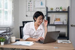 © Wasana - Cheerful businesswoman in white shirt using smartphone with laptop and documents on her office desk.