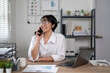 © Wasana - Cheerful businesswoman in white shirt using smartphone with laptop and documents on her office desk.