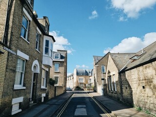 Cambridge back street in England with narrow alley between historic building walls under cloudy sky