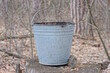 one old gray metal bucket stands on a wooden stump on the street