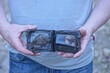 hands of a man in gray clothes holding an old open black leather wallet on the street