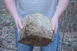 man's hands holding one large gray concrete piece of stone on the street