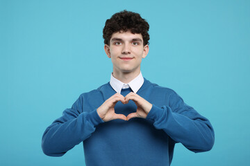 Wall Mural - Happy young man showing heart gesture with hands on light blue background