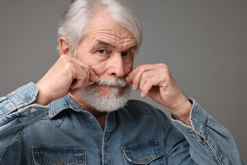 Wall Mural - Senior man touching mustache on grey background