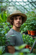 Young Male Gardener in Straw Hat Standing Among Greenhouse Plants