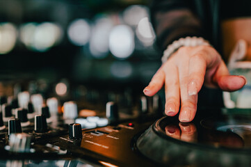 Wall Mural - Close-up of a DJ’s hand adjusting audio equipment in a dimly lit setting, with blurred lights in the background, creating a vibrant atmosphere