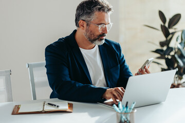 Focused businessman using laptop and smartphone in office