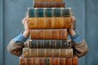 A person's arms are seen holding a tall stack of antique books, evoking the love for literature and knowledge