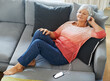 Senior woman and headphones, music with phone on sofa for relax and rest in living room. Mature, female person and smartphone for listening or streaming podcast on couch for peaceful retirement