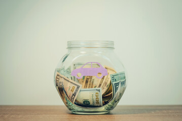 Toned photo of transparent glass money box, dollar banknotes inside, picture of car on it, toned, close up. Saving money for new vehicle, concept of reaching financial goals