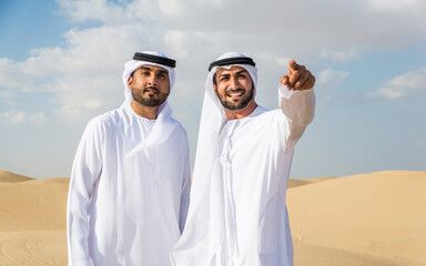 Wall Mural - Two arab men wearing traditional emirati clothing in the desert of Dubai - Middle-eastern adult males portrait