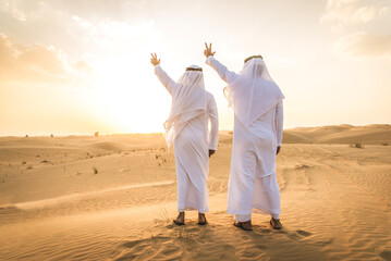 Wall Mural - Two arab men wearing traditional emirati clothing in the desert of Dubai - Middle-eastern adult males portrait