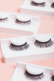 Fototapeta Tulipany - Different fake eyelashes in boxes on trendy pastel pink background. Makeup accessories and beauty cosmetics products for women. Top view, flat lay.