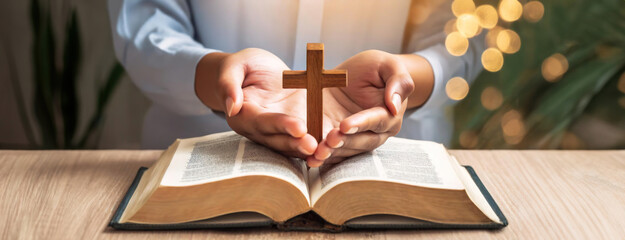 Priest hands hold a wooden cross over an open bible. Sense of devotion and prayer.
