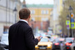 Man in a business suit standing with smartphone on a street on cars background. Using mobile phone in city