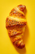 Croissant with sesame seeds on yellow background.