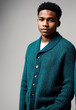 A young man wearing a green sweater and standing in front of a gray background.