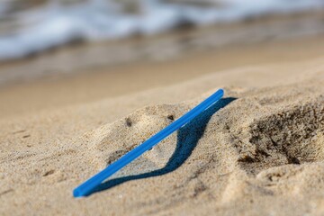 Blue straw on the beach sand, concept of plastic waste, recycling, pollution prevention, environmental conservation.