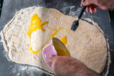 Fototapeta Uliczki - Teig wird in der Küche mit geschmolzener Butter und Zimt bestrichenaus einem rosa Topf gehalten von Männer Hand