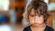 A young child with curly hair is looking down with a sad expression. The child is wearing a black shirt and he is wet