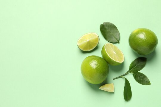 whole and cut fresh ripe limes with leaves on light green background, flat lay