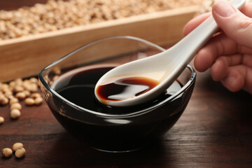 Woman taking soy sauce with spoon from bowl at wooden table, closeup