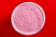 Raspberry banana smoothie in glass on a red background, closeup, top view
