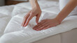 © Vero - Woman s hands putting white fitted sheet on bed over mattress on bed.