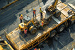 Workers secure heavy machinery onto flatbed trailers at a construction site.
