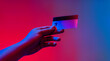 A hand holding a credit card to make an electronic payment against a blue and pink gradient background.