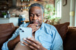 © Marko Geber - Senior black man using smartphone on the couch