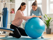 © acnaleksy - physiotherapist helping female patient to do exercise on fitness ball in physio room