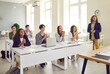 © Studio Romantic - High school teenagers enjoy interesting class. Group of happy smiling adolescent students sitting at white desks in modern light classroom interior, looking away and applauding together with teacher