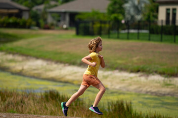 Canvas Print - Young kid running and smiling in the park. Active little kid running along street during leisure sport activity. Sporty kid running in nature. Child run. Kids running. Summer sport. Happy childhood.