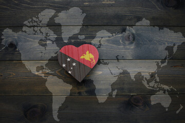 Wall Mural - wooden heart with national flag of Papua New Guinea near world map on the wooden background.