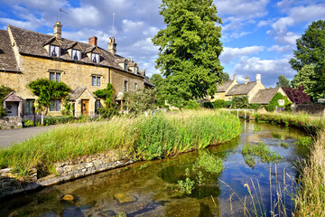 beautiful cotswolds village of lower slaughter with river under blue skies, gloucestershire, england