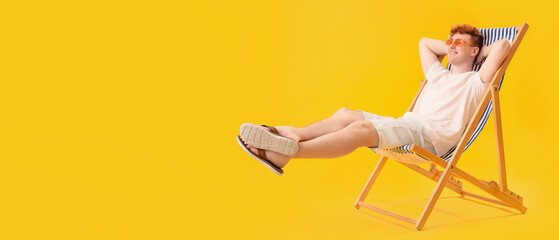 Wall Mural - Young man resting in deck chair on yellow background