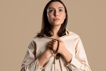 Wall Mural - Young woman praying with beads on beige background, closeup