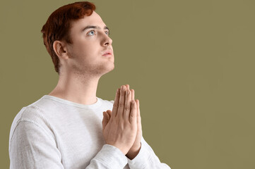 Wall Mural - Young man praying on green background, closeup