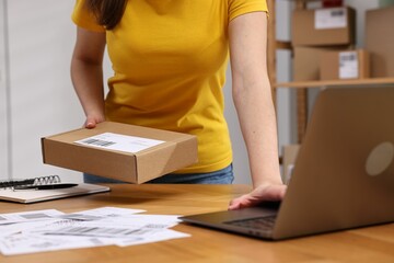 Sticker - Parcel packing. Post office worker with box using laptop at wooden table indoors, closeup