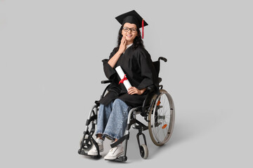 Wall Mural - Beautiful female graduate student in wheelchair with graduation cap and diploma on grey background