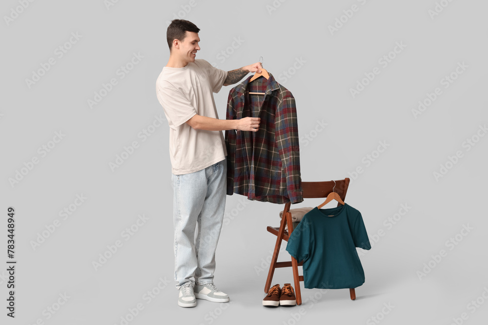 Handsome young man and chair with clothes on grey background