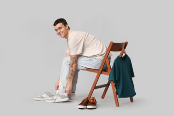 Wall Mural - Handsome young man and chair with clothes on grey background