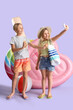 Cute little kids with inflatable mattresses and starfishes taking selfie on lilac background