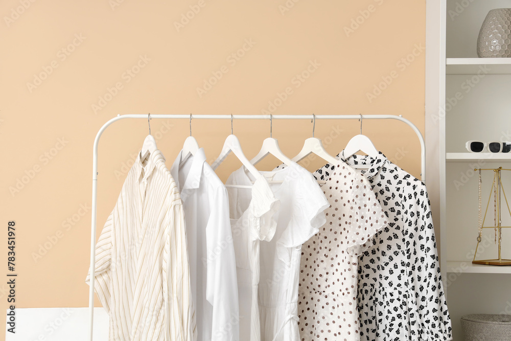 Stylish female clothes hanging on rack near color wall