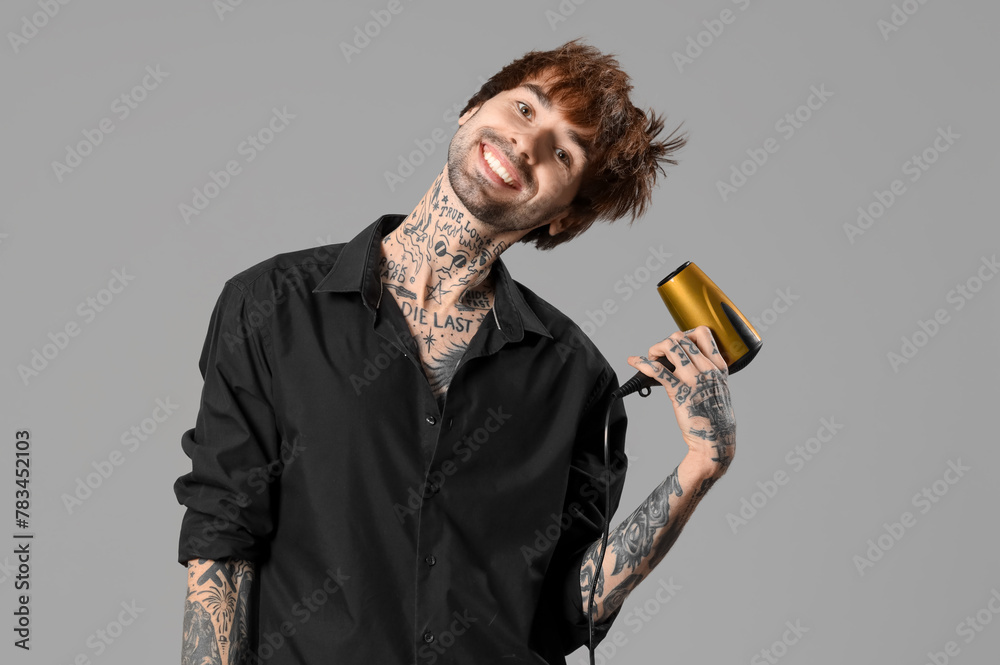 Young tattooed barber drying hair on grey background